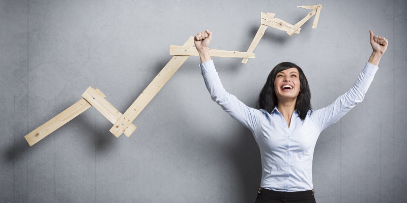 Concept: Success in business or career. Enthusiastic businesswoman with raised arms cheering in front of positive business graph, isolated on grey background.